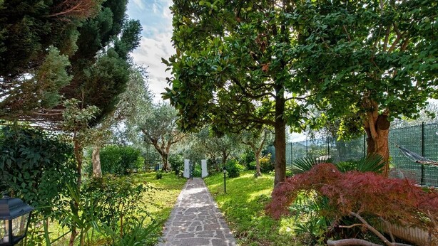 A stone pathway in a lush garden with various trees and plants. - Apartment 'Solarolo Cristina' with Lake View, Wi-Fi and Air Conditioning (Solarolo)