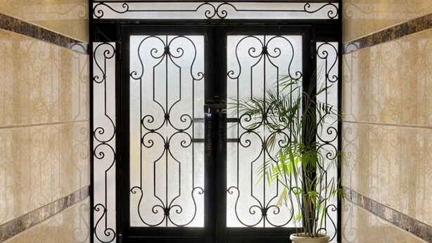Un vestíbulo con piso de mármol pulido, una puerta decorativa grande con detalles de metalería y una araña.