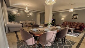 Un comedor con una mesa redonda dispuesta para cuatro personas, rodeada de sillas. Hay dos sofás, una mesa de centro y un televisor al fondo.