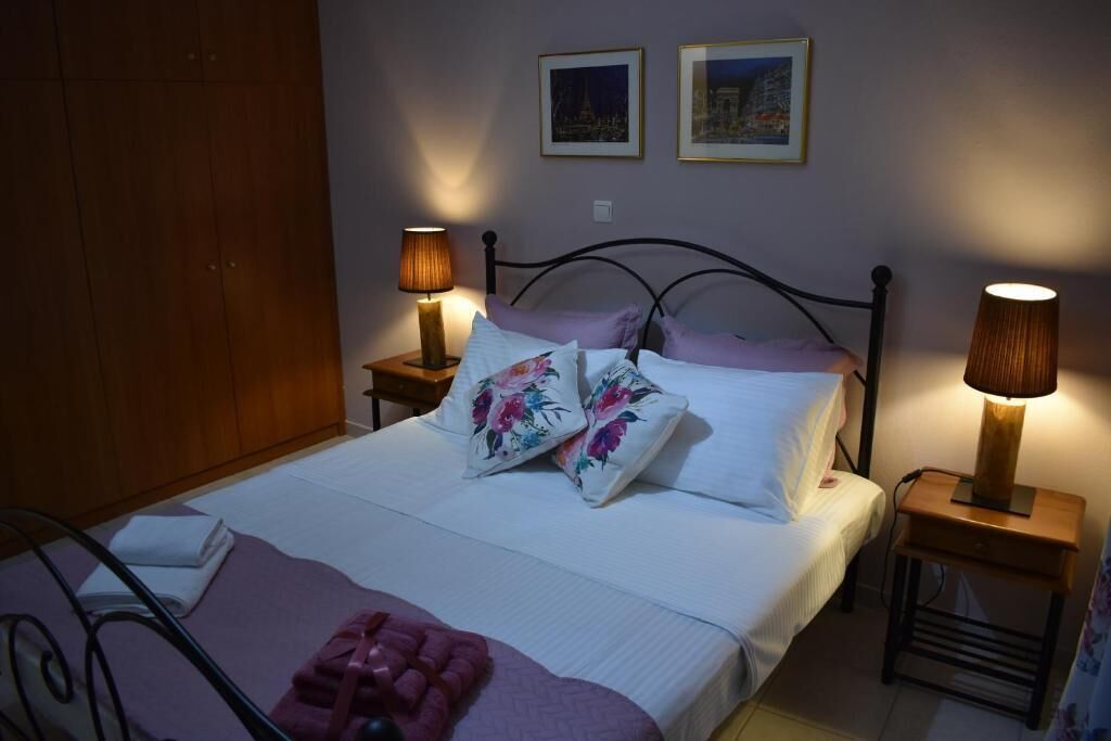 A neatly made bed with floral pillows and a pink blanket, two bedside lamps, and two framed pictures on the wall.