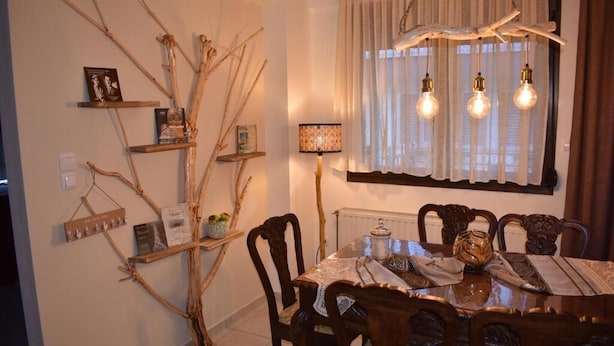 Un coin repas avec une table en bois, des chaises et un lustre. Des étagères sont fixées au mur et accueillent des livres et des objets décoratifs.