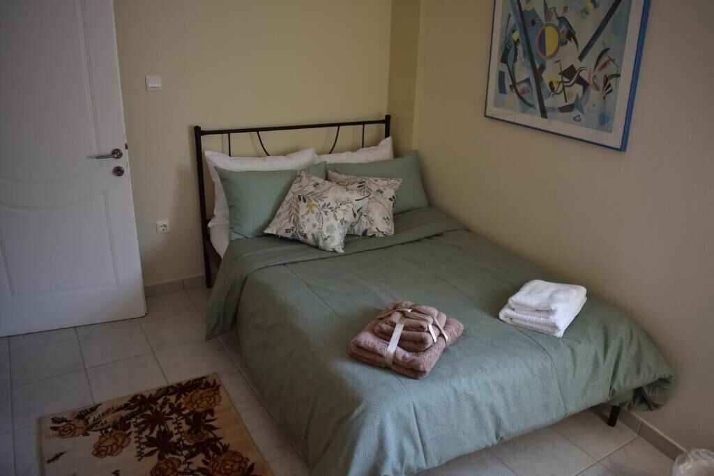 A single bed with a green bedspread and pillows, a small rug, and a painting on the wall.