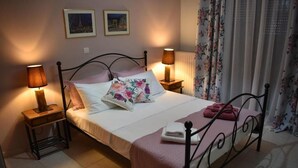 Un lit bien fait, agrémenté d’un coussin à motifs floraux, de deux lampes de chevet et d’une couverture rose.