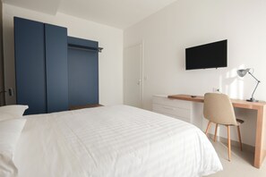 A bedroom with a bed, a desk, a chair, a TV, and a wardrobe.