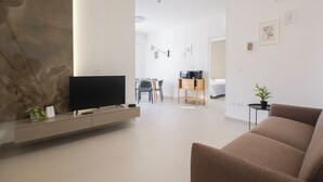 Una sala de estar moderna con televisión de pantalla plana, un sofá, una mesa de centro y un comedor con sillas y una pequeña mesa.