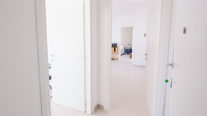Un pasillo con paredes blancas y puertas que dan a una habitación con cama y mesita de noche.