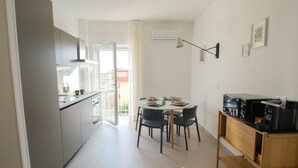 Una cocina moderna con armarios grises, un área de comedor con una mesa redonda y sillas, y una cafetera sobre un pedestal de madera.