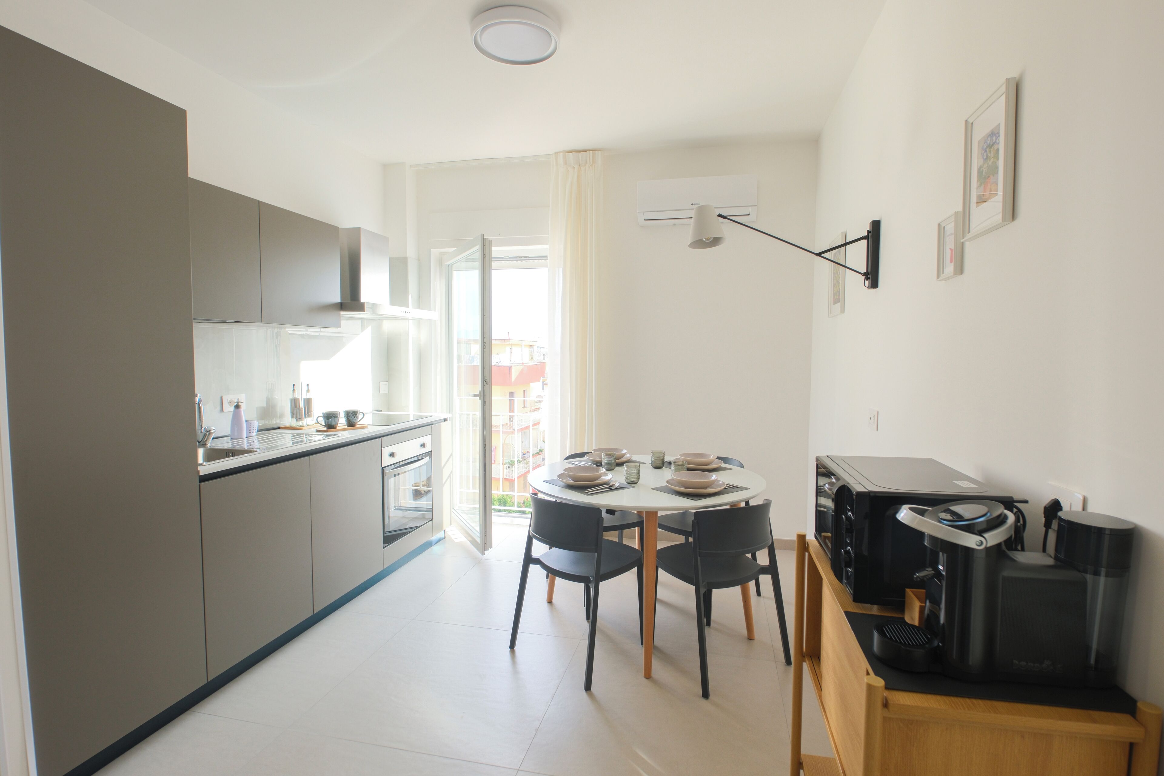 A modern kitchen with grey cabinets, a dining area with a round table and chairs, and a coffee machine on a wooden counter.