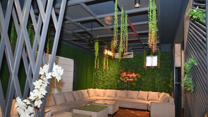 Ein moderner Lounge-Bereich mit Ecksofa, hängenden Pflanzen und einer grünen Wand mit einer Neonreklame.