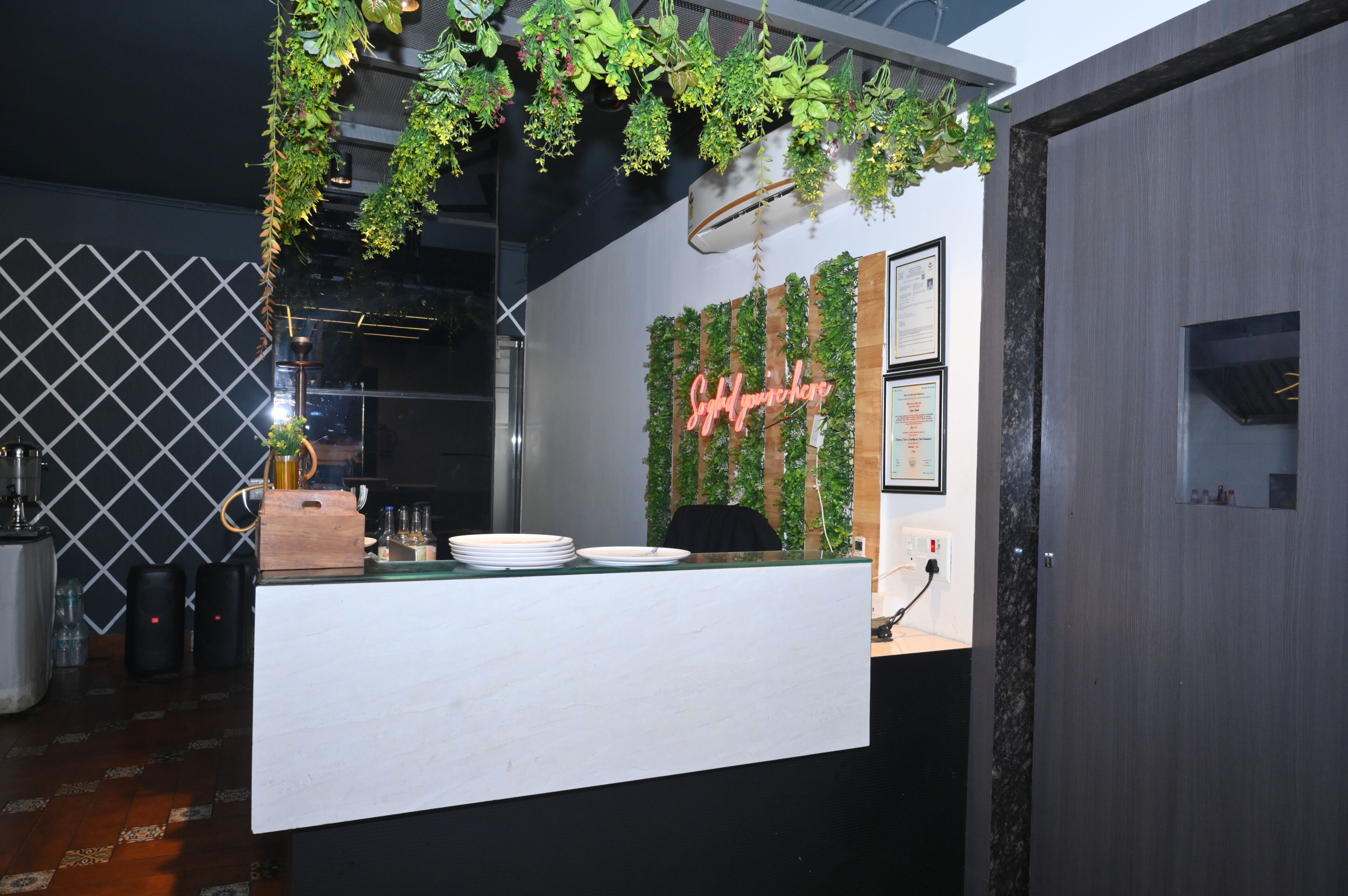 Un área de recepción moderna con un mostrador blanco, plantas colgantes y un letrero de neón.