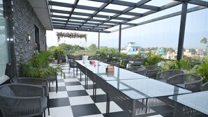 Eine Dachterrasse mit Schachbrettboden, Glastischen, Korbstühlen und Topfpflanzen.