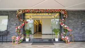 Ein Hotel mit Eingangsbereich, einem Blumenschmuckbogen, Topfpflanzen und einem modernen Innenraum, der durch die Glasüren sichtbar ist.