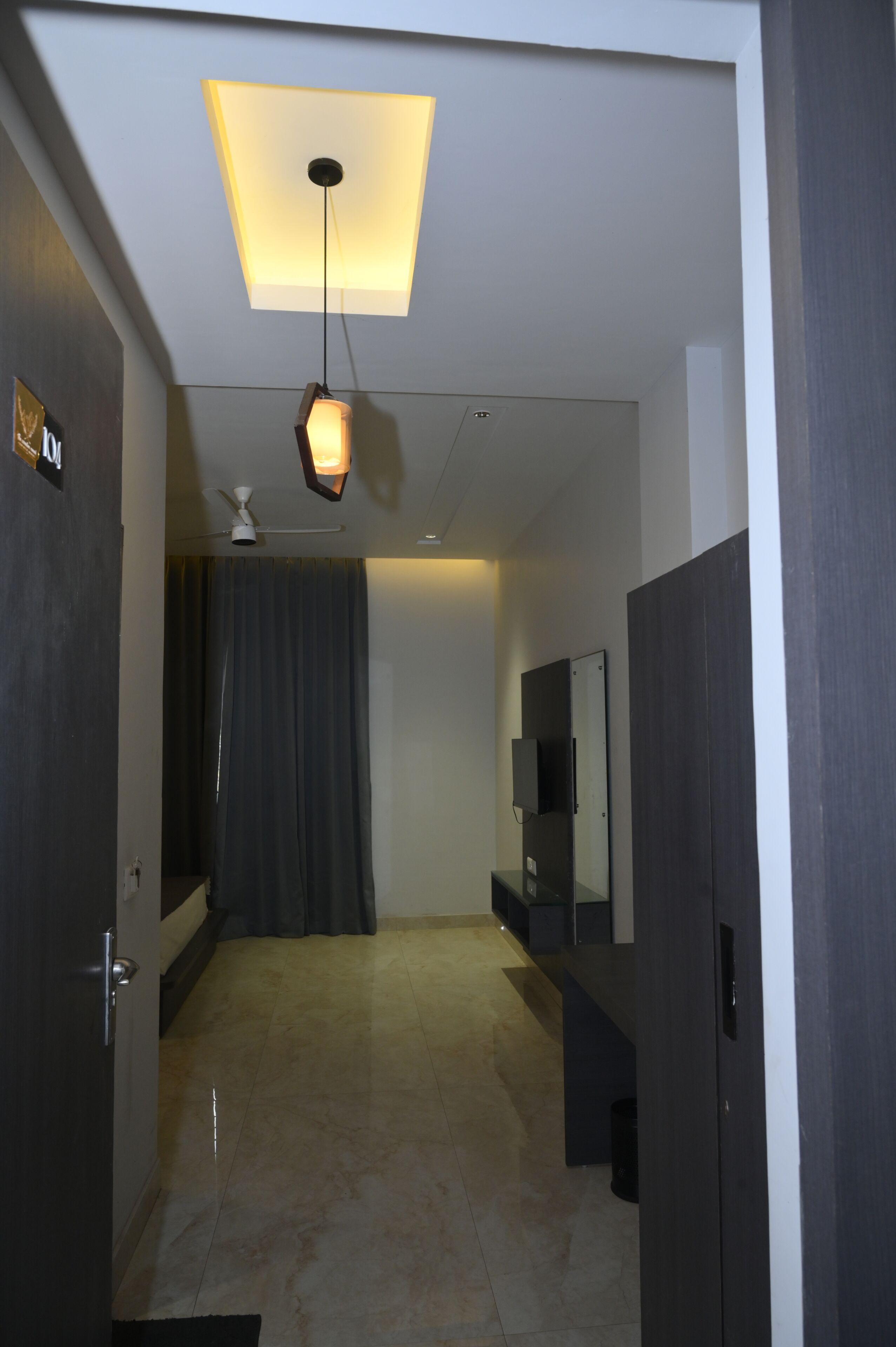 A hallway with a ceiling light, a ceiling fan, a dark curtain, a mirror, and a door.