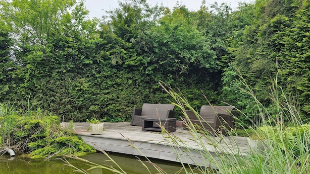En træterrasse med udendørs møbler med udsigt over en sø, omgivet af frodig vegetation.
