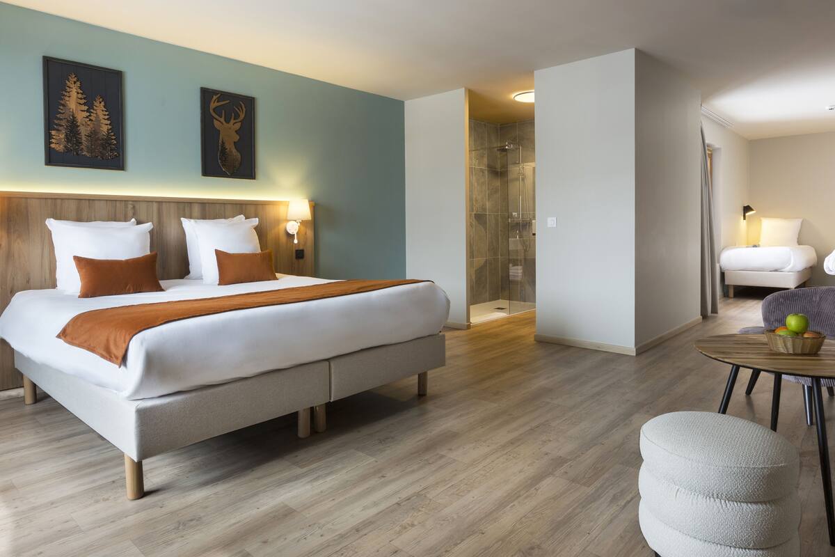 A modern hotel room with a large bed, a shower, a dining area, and a seating area.