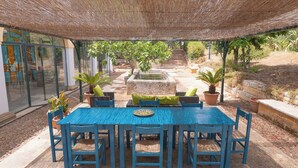 Eine Terrassengruppe im Freien mit blauem Tisch und Stühlen, umgeben von Topfpflanzen und einem Steinfountain.