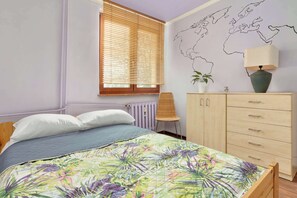 A bedroom with a bed, a world map on the wall, a window with blinds, a chair, a dresser, and a lamp. - Spacious Apartment | 4 Bedrooms | 1.5 km to the Beach (Gdańsk)
