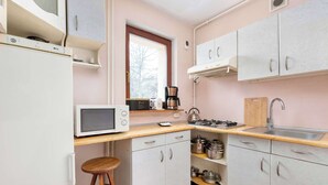 Ett kompakt kök med vita skåp, en mikrovågsugn, en kaffebryggare och en gasspis.