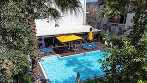 A swimming pool with blue water, surrounded by lounge chairs and umbrellas, with a building and trees in the background. - Hotel Ena - Cozy Mountain View Suite with Pool (Loutra Ypatis)