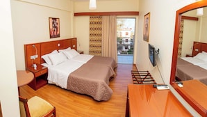 A hotel room with two beds, a desk, a chair, a TV, and a balcony with a patterned curtain. - Hotel Ena - Cozy Mountain View Suite with Pool (Loutra Ypatis)