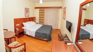Hotellihuone, jossa on sänky, yöpöytä, tuoli, televisio ja peili.