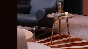 A modern lounge area with a black leather sofa, a small wooden table with a glass, and a patterned rug. - Pudong airport W9 hotel Shanghai (Shanghai)
