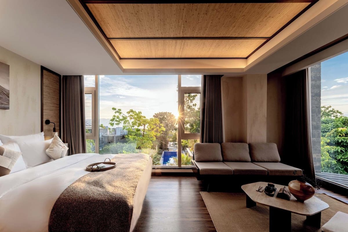 Een moderne hotelkamer met een groot bed, een bank, een bijzettafeltje en uitzicht op het landschap.