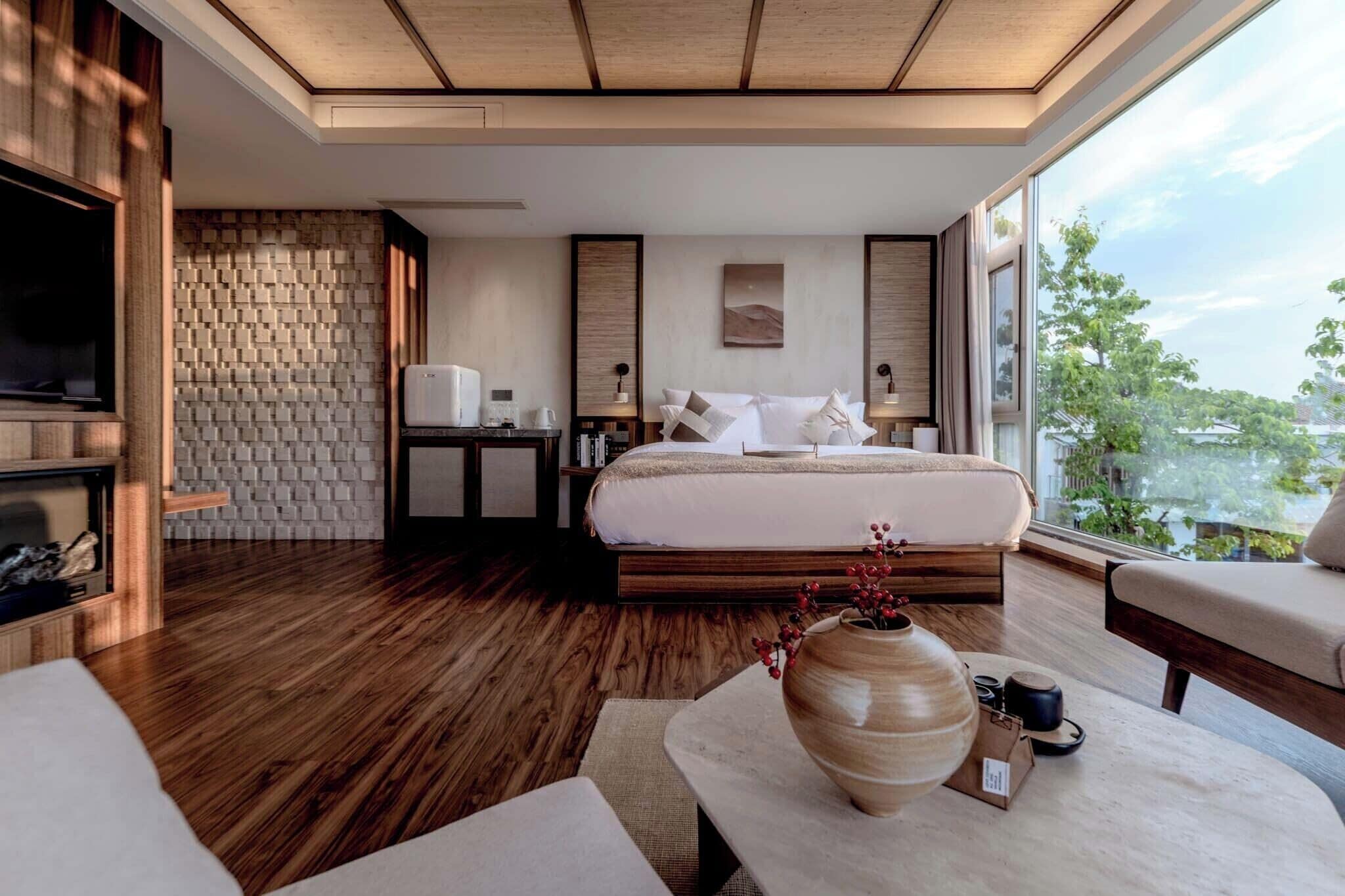 Habitación de hotel moderna con una cama grande, zona de estar, chimenea y vistas al exterior.