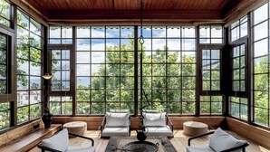 Ein sonnendurchflutetes Zimmer mit großen Fenstern, Holzboden und modernen Möbeln, darunter zwei Sofas und ein runder Tisch.