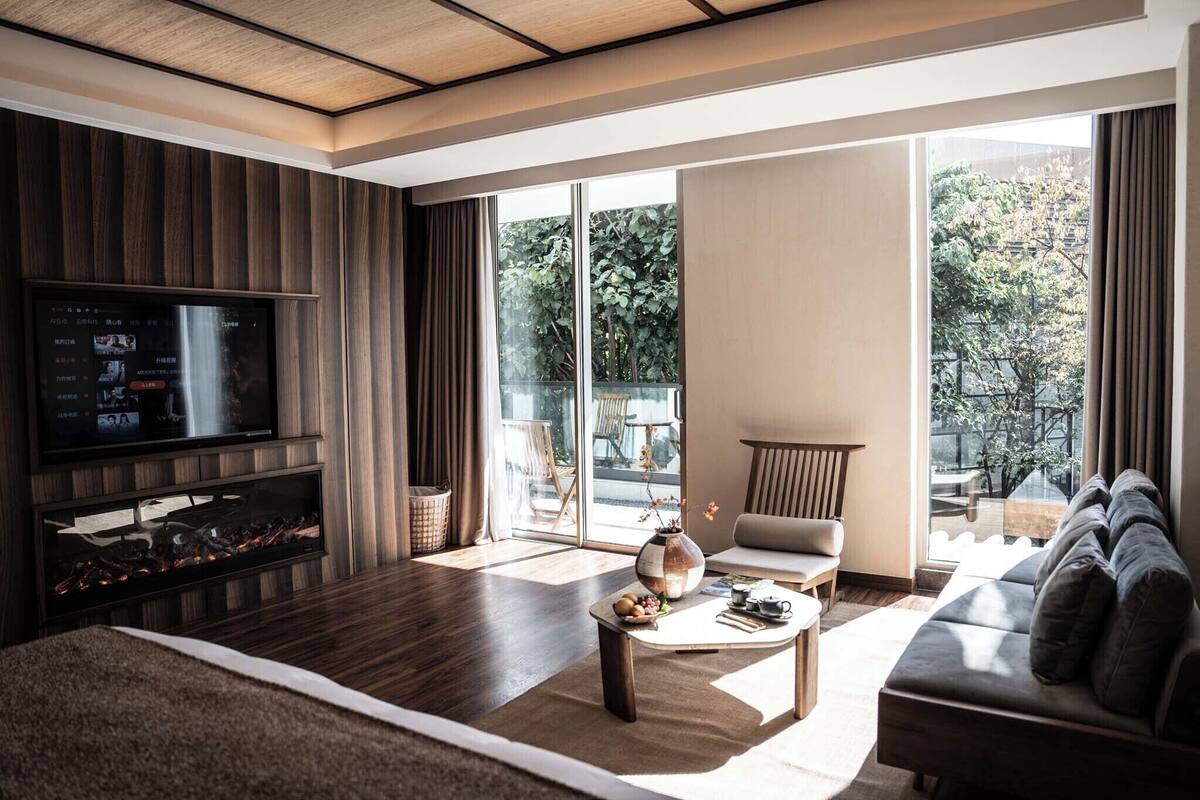 Een moderne woonkamer met een flatscreen televisie, een open haard, een bank, een salontafel en grote ramen met uitzicht op het landschap.