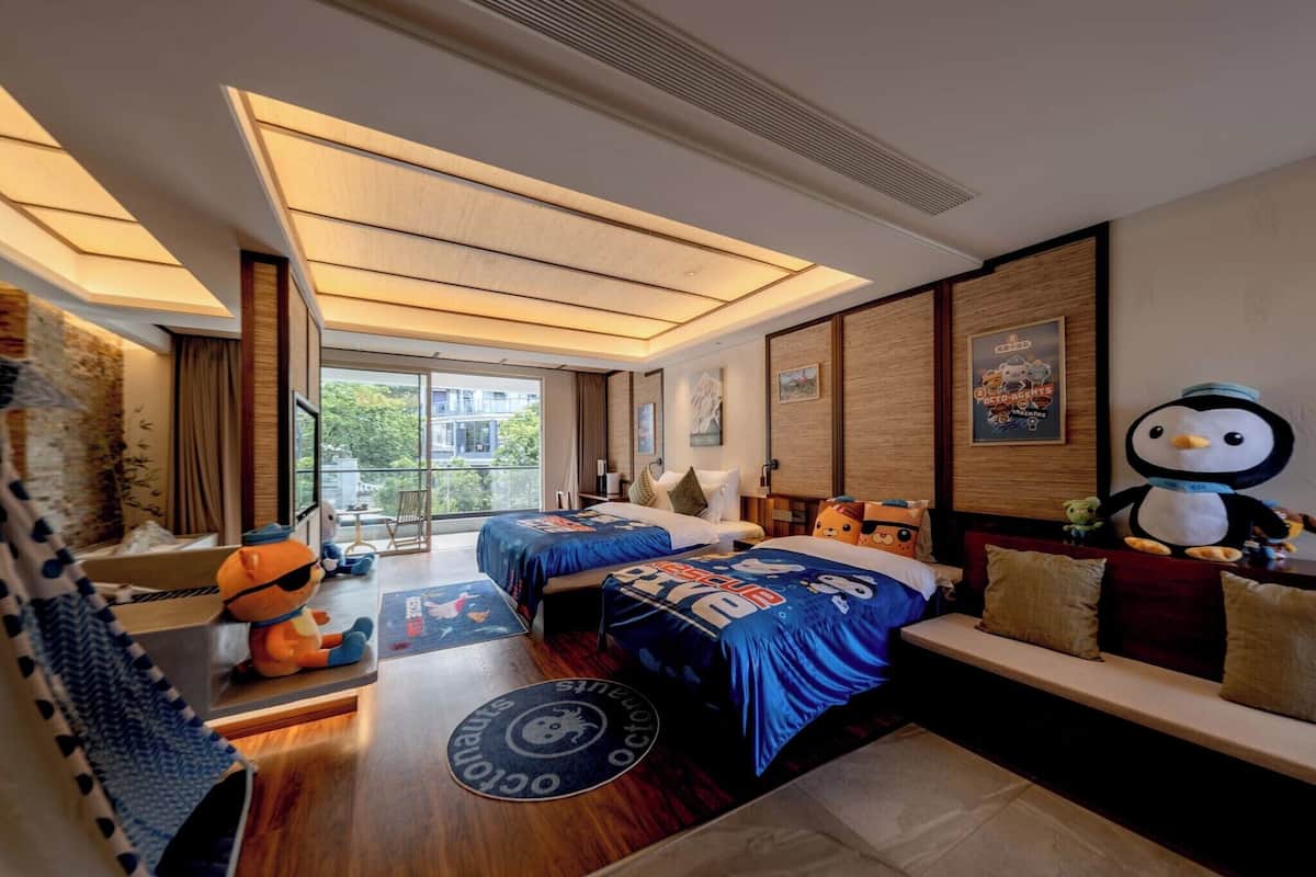 Een hotelkamer met twee bedden, een slaapbank, een groot raam en uitzicht op groen.