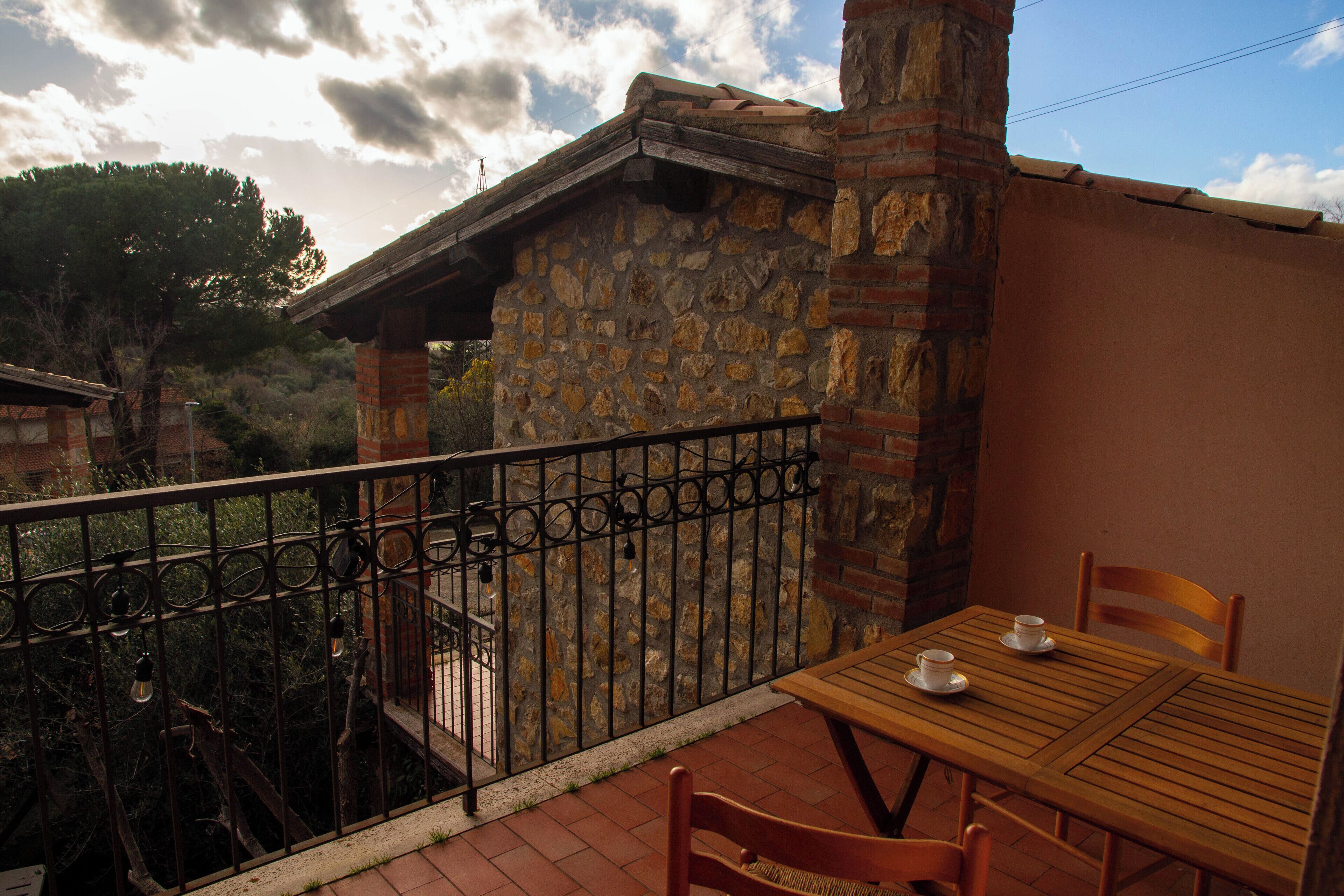 A stone building with a balcony, a wooden table with chairs, and a metal railing.