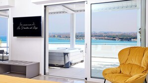 Quarto moderno com uma cama, uma poltrona amarela, uma TV e uma porta de vidro deslizante para uma varanda com vista para a cidade.