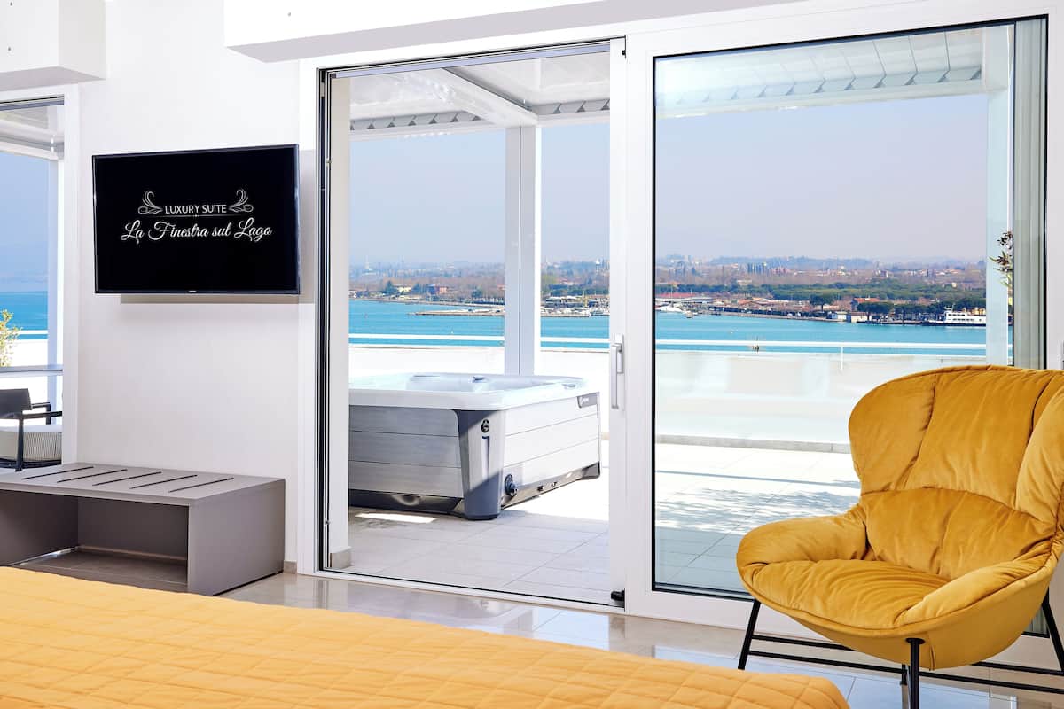 Ein modernes Zimmer mit einem Bett, einem gelben Sessel, einem Fernseher und einer Glastür, die auf einen Balkon mit Blick auf die Stadt führt.