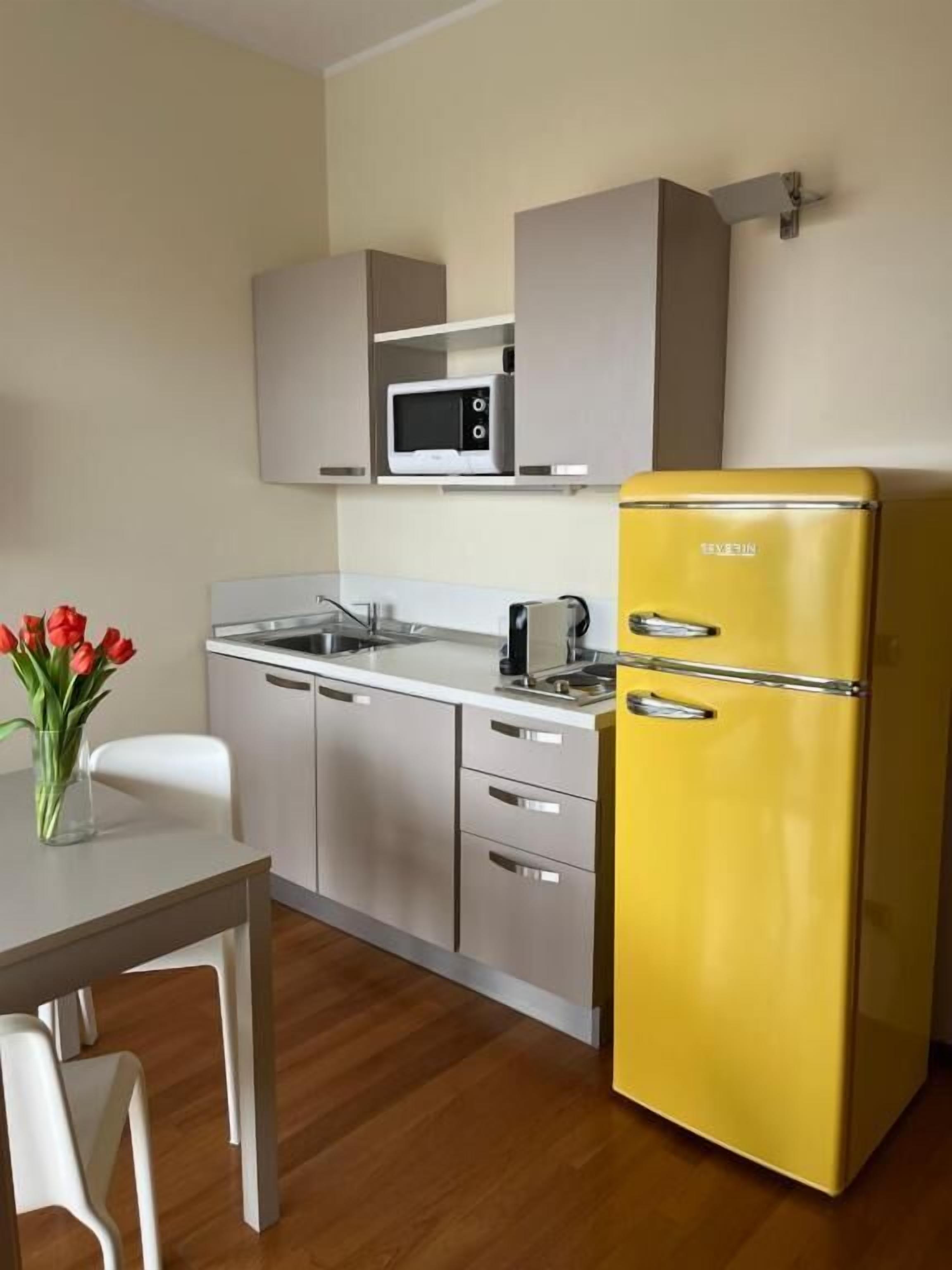 Une cuisine de taille réduite, avec un réfrigérateur jaune, un four à micro-ondes et une machine à café posés sur le plan de travail.