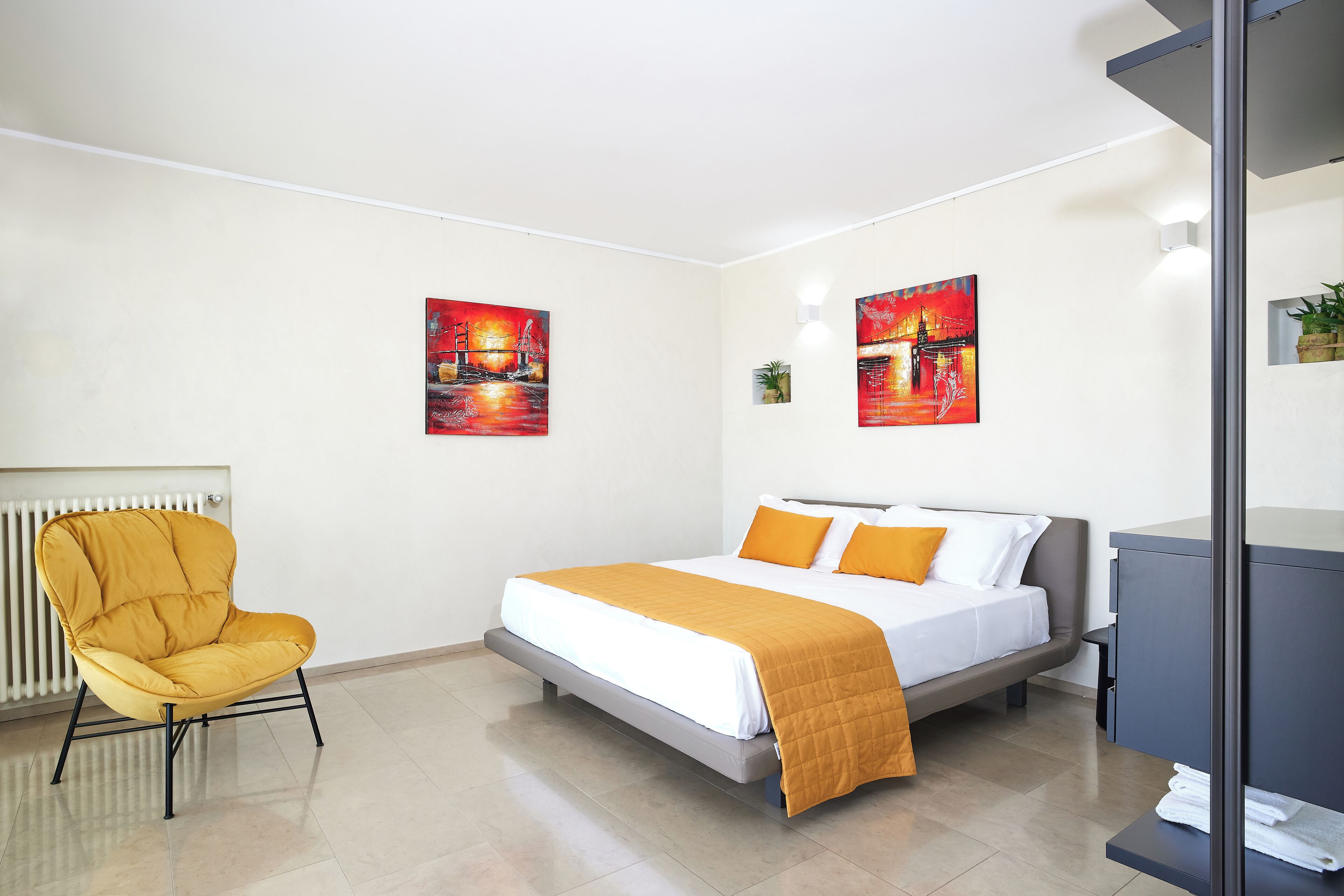 Una habitación de hotel moderna con una cama, un sillón amarillo y dos cuadros en la pared.