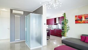 Uma sala de estar moderna com um sofá cinzento, um banquinho vermelho e um painel de vidro.