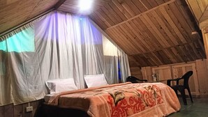 Kodikas ullakkohuone, jossa on sänky, kaksi tuolia ja pieni pöytä.