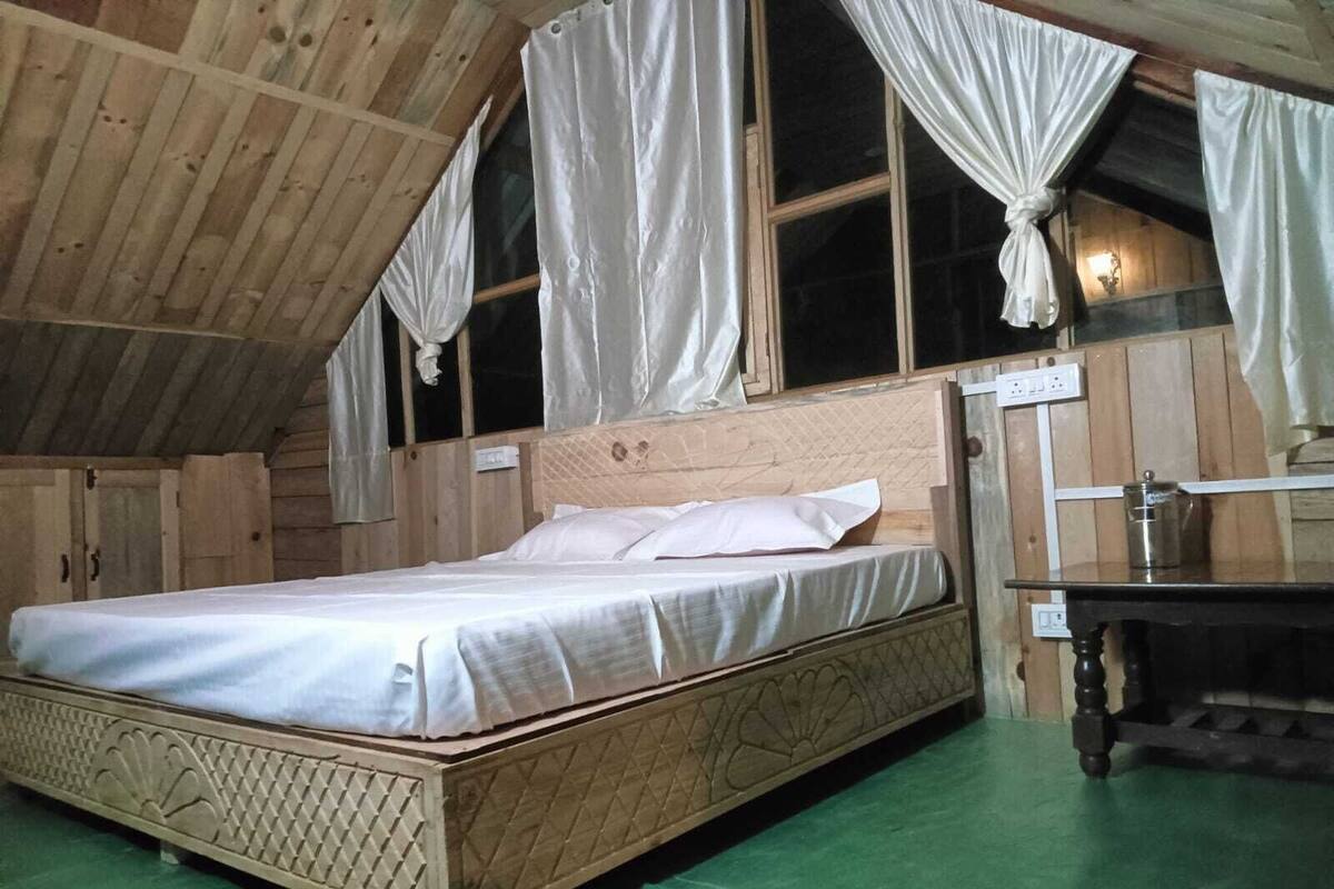 Camera da letto in una baita di legno con un letto, tende e un tavolino.
