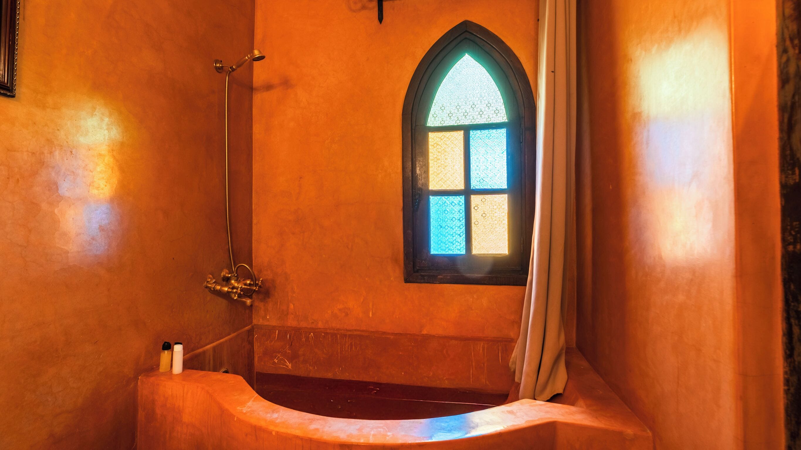 A bathroom with a bathtub, a shower, and a stained glass window.