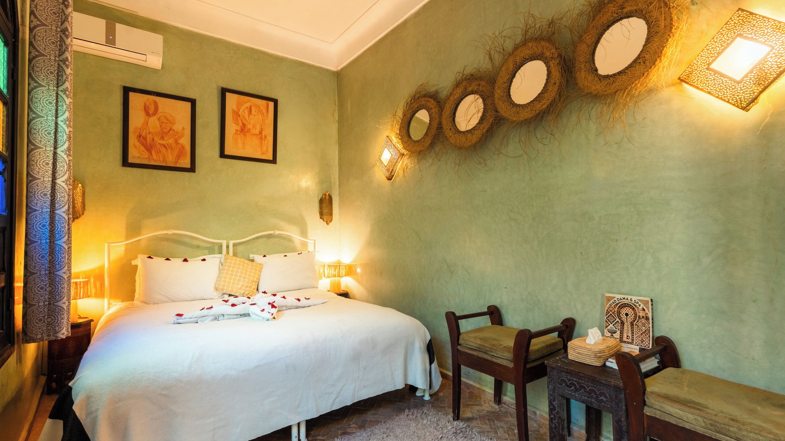 Un dormitorio con cama, lámparas de noche, una silla, una mesita y espejos en la pared.
