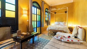 Ein Zimmer mit einem Himmelbett, einem Schreibtisch und einem Stuhl sowie einem gemusterten Teppich.