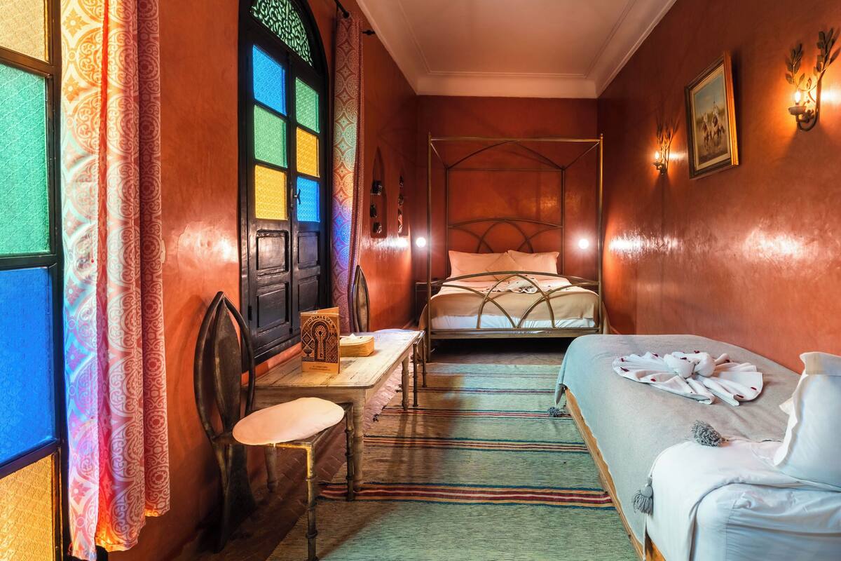 A narrow room with a bed, a small table, and a chair.