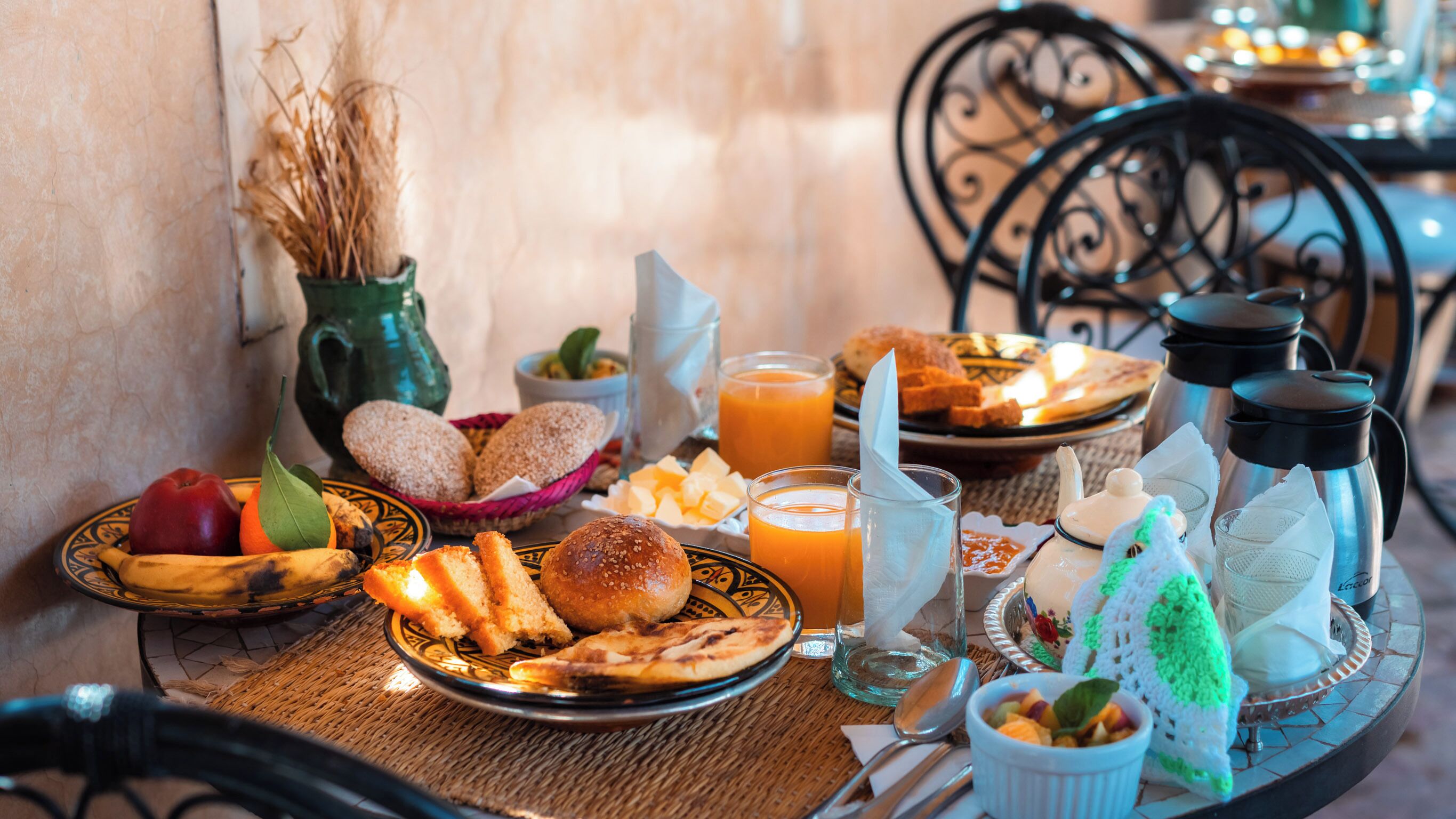 Una mesa de desayuno con pan, pasteles, fruta y bebidas.