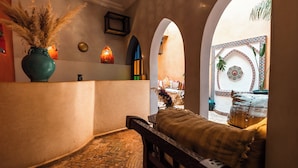 Ein gemütliches Interieur mit einer Bank, einer Vase mit Trockenblumen, einem an der Wand befestigten Regal mit Dekoration und einer gemusterten Wand.