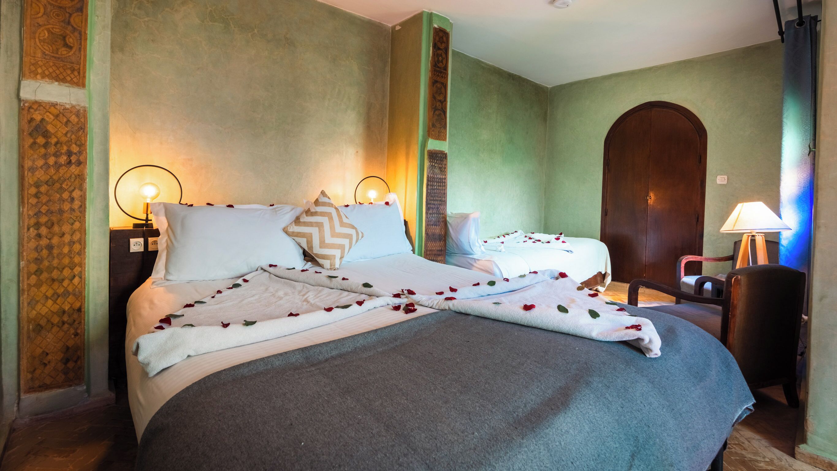 Quarto de hotel com duas camas, uma porta de madeira, uma cadeira e um abajur.
