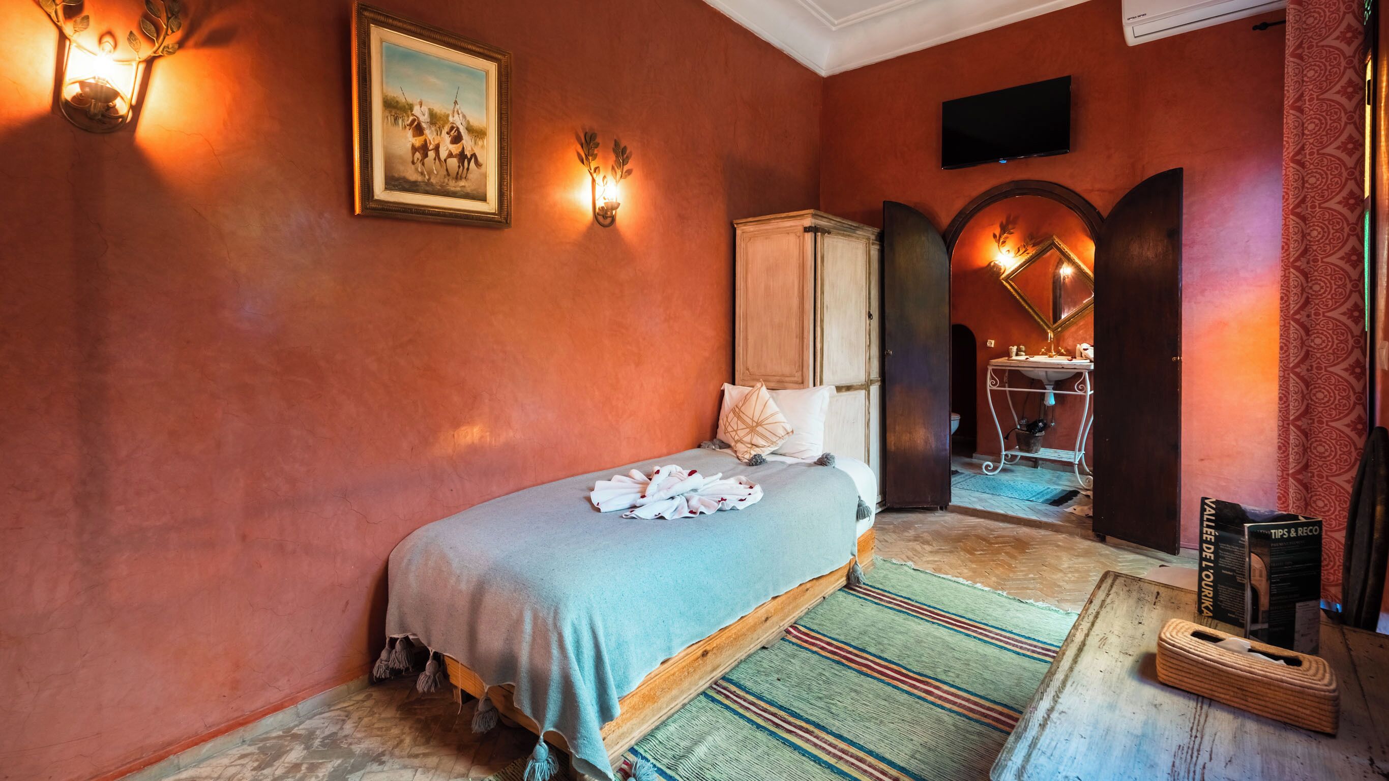 A bedroom with a bed, a painting, a wardrobe, a mirror, and a television.
