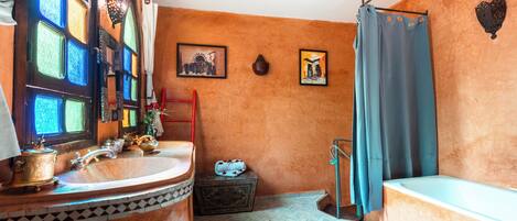 Une salle de bain avec un meuble-lavabo en bois, une baignoire, un rideau de douche et deux tableaux encadrés au mur.