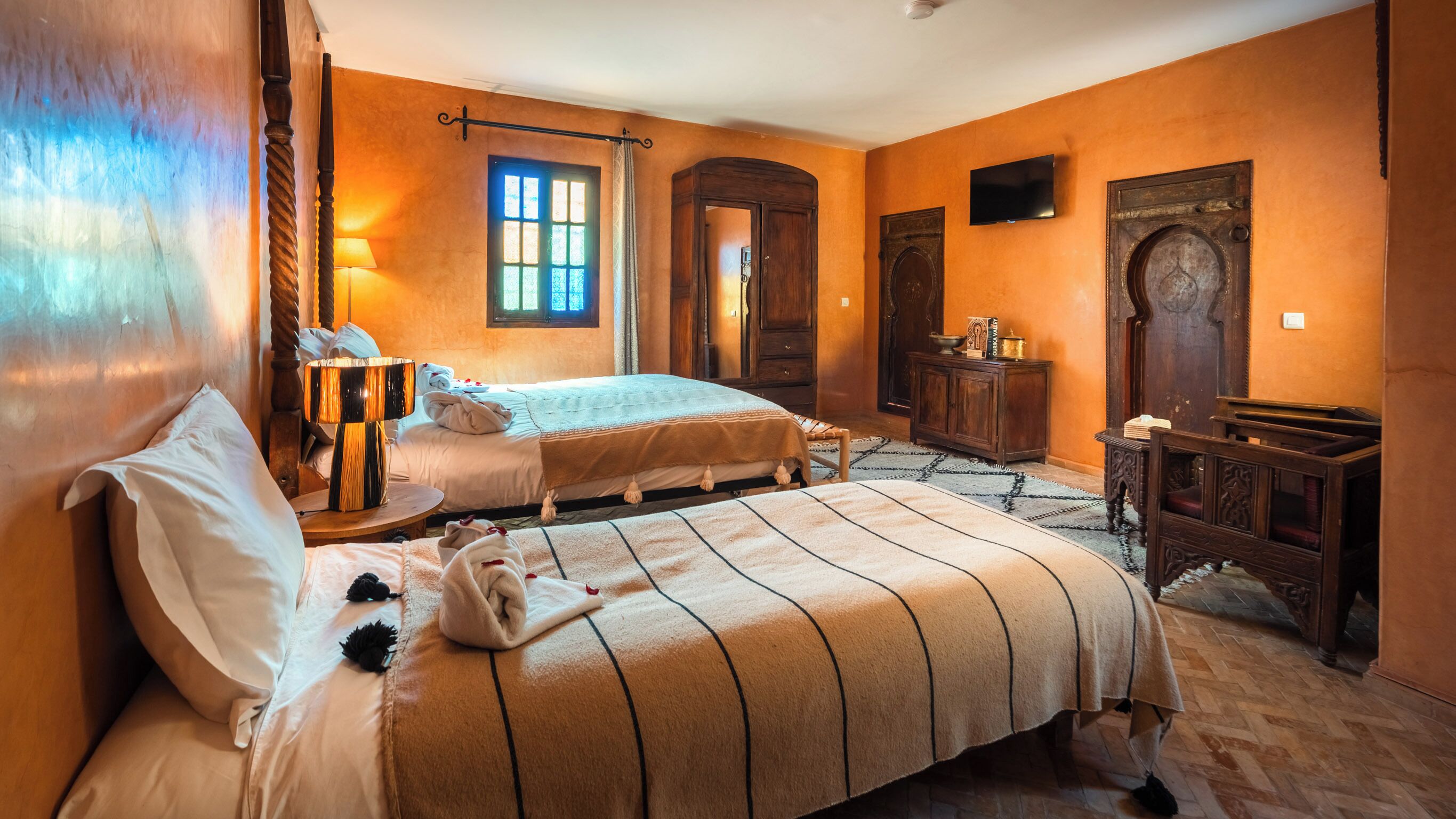 Una habitación con cama, mesita de noche, lámpara, armario y televisor.
