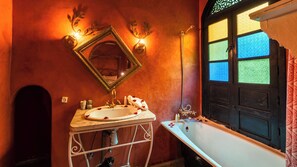 A bathroom with a white sink, a mirror, a bathtub, and a window with patterned glass. - Riad Dama & SPA (Marrakech)